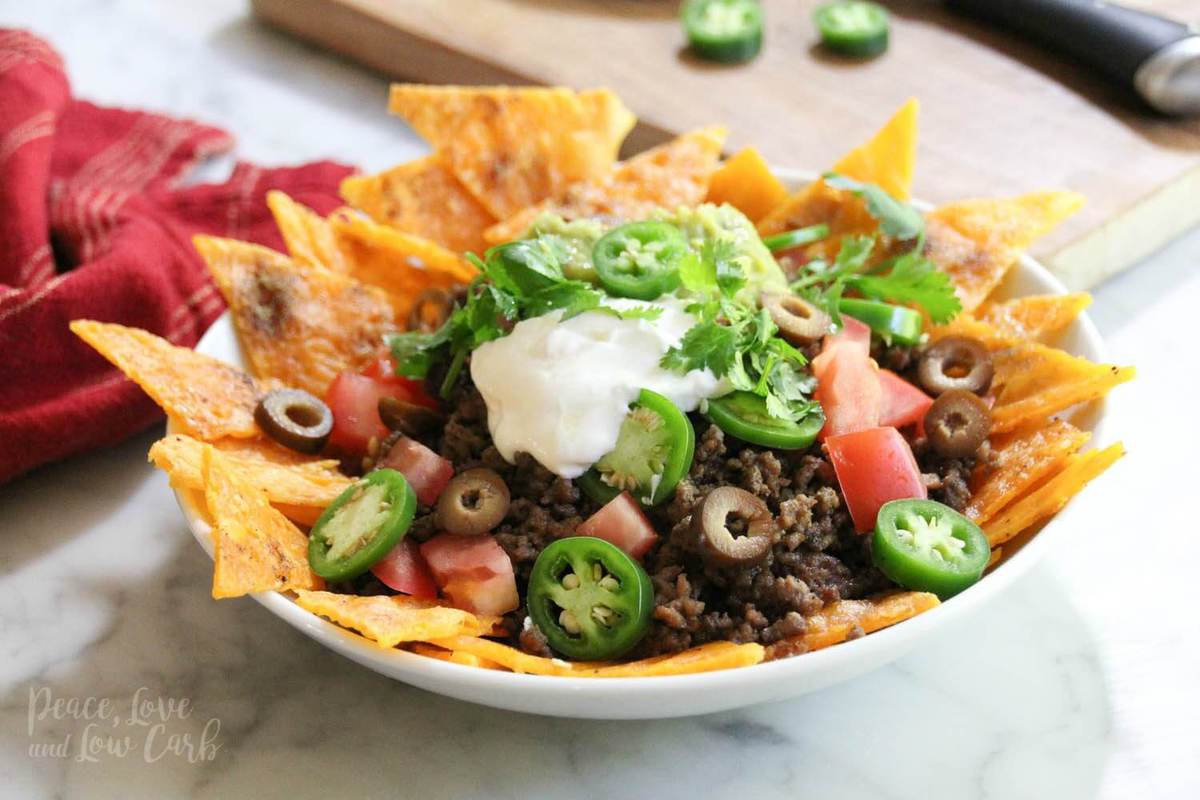 a plate of low carb chips made out of cheese, topped with beef, onions, olives, tomatoes, jalapeños, sour cream and cilantro