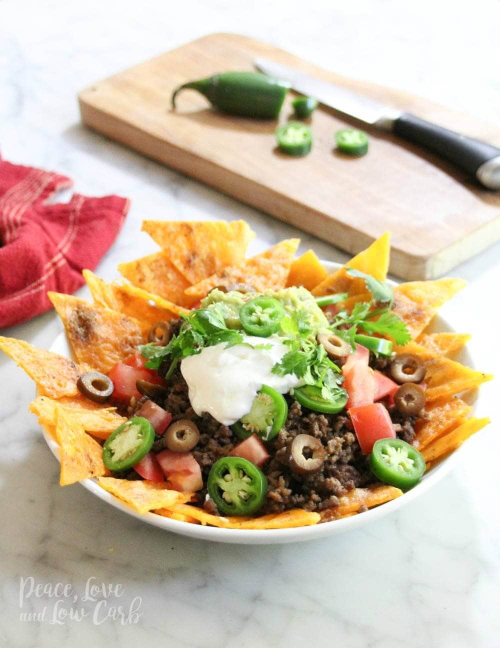 a plate of low carb chips made out of cheese, topped with beef, onions, olives, tomatoes, jalapeños, sour cream and cilantro