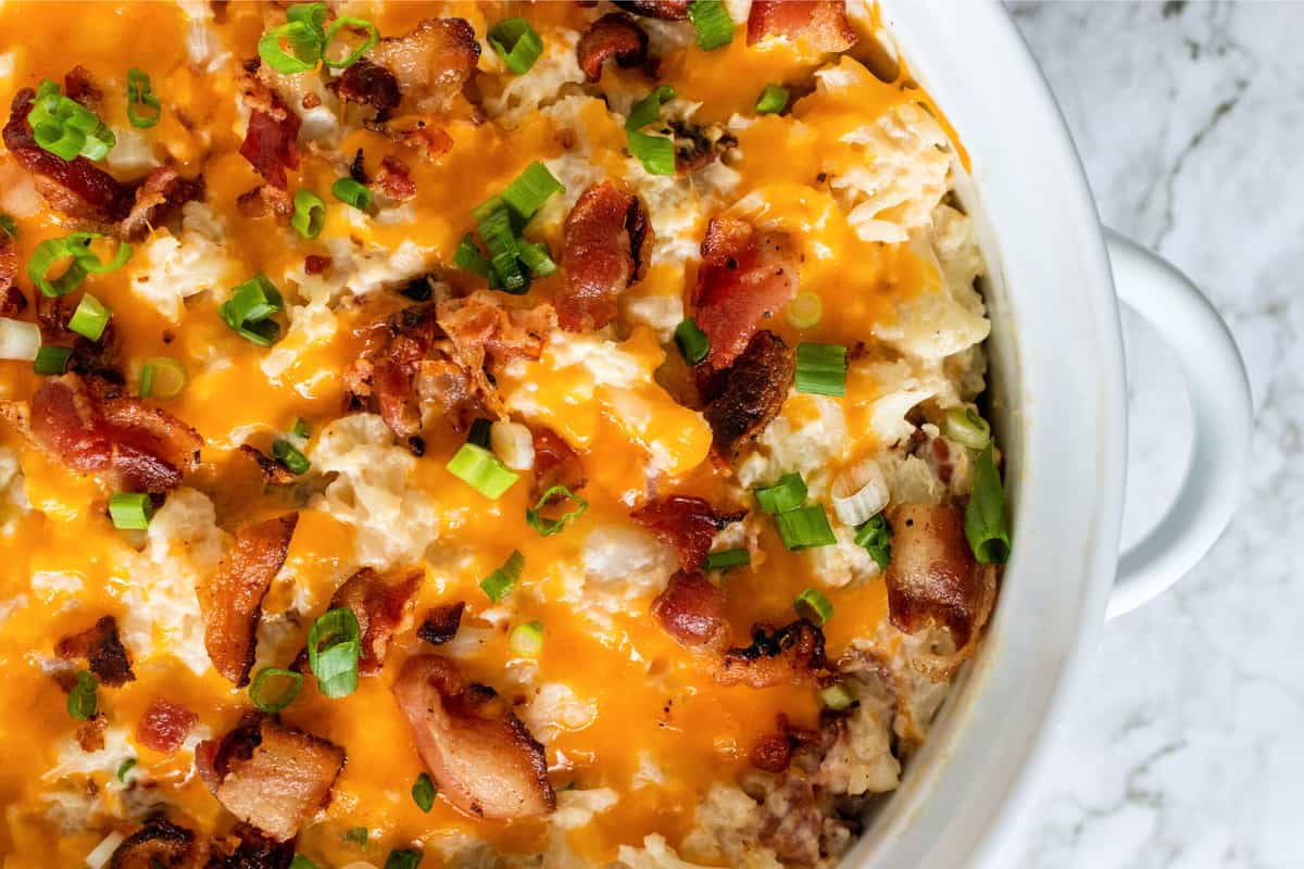 white casserole dish with a twice baked cauliflower with bacon, cheese, and green onions