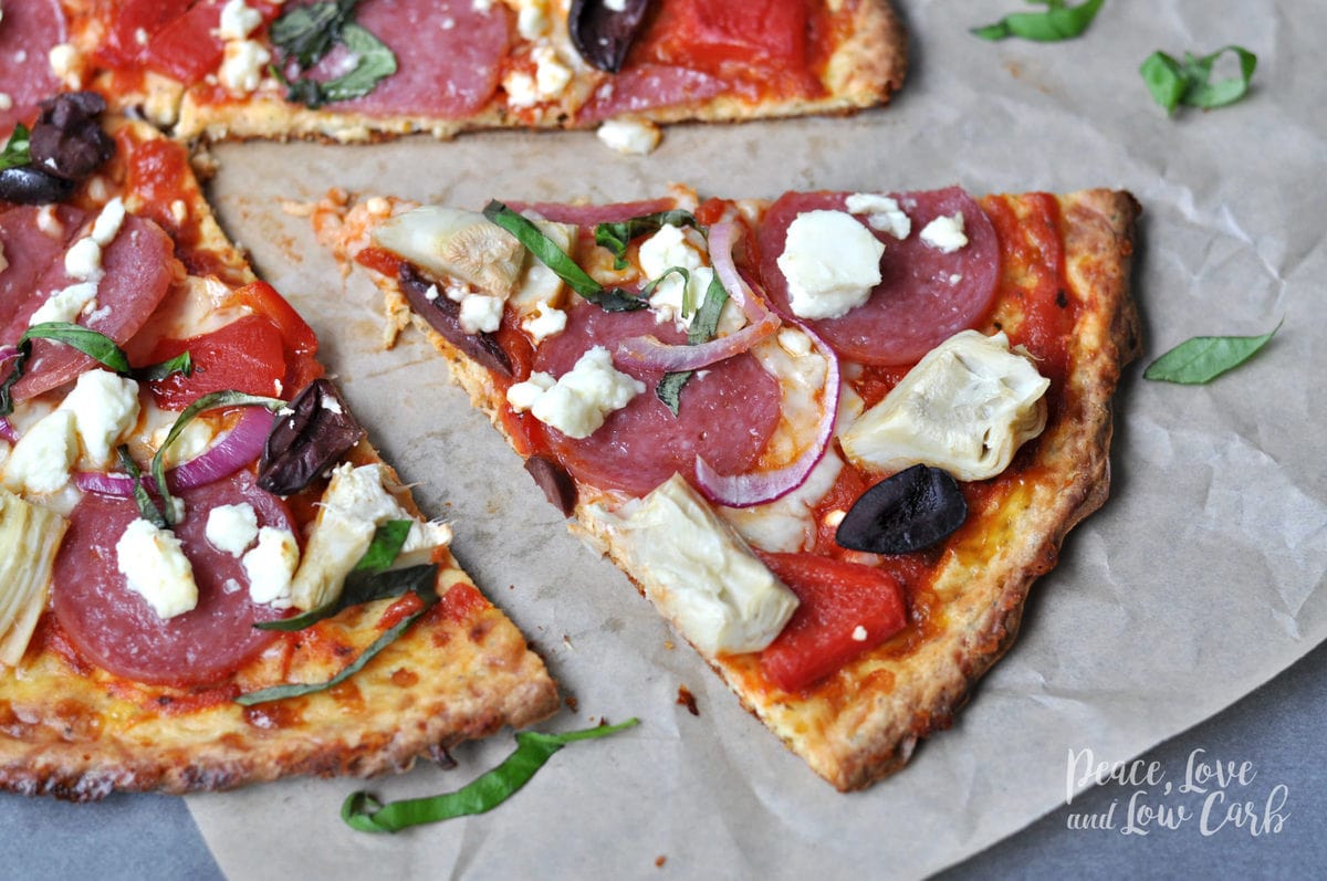 a keto greek pizza, topped with salami artichokes, olives, feta, onions, basil and peppers