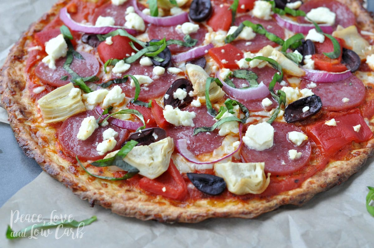 a close up shot of a keto greek pizza, topped with salami artichokes, olives, feta, onions and peppers