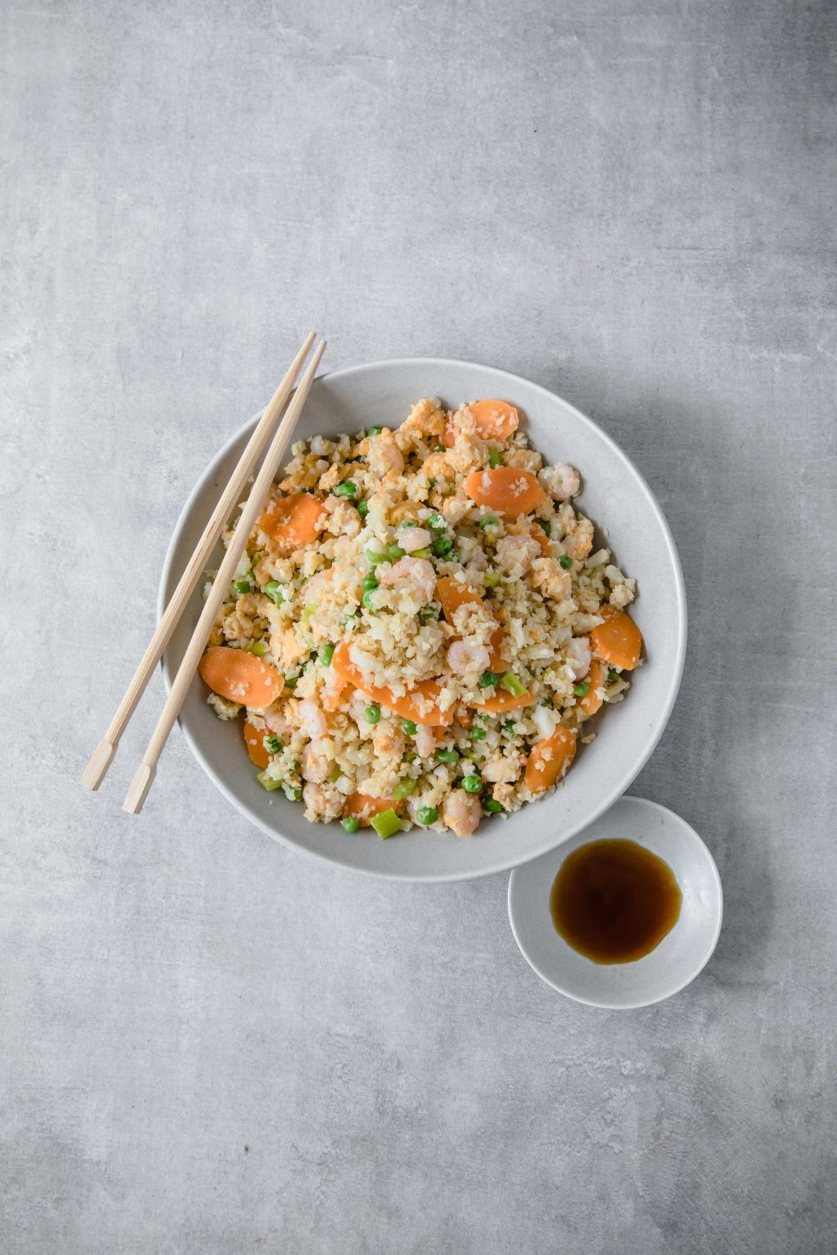 A white bowl filled with cauliflower fried rice with shrimp, carrots and peas