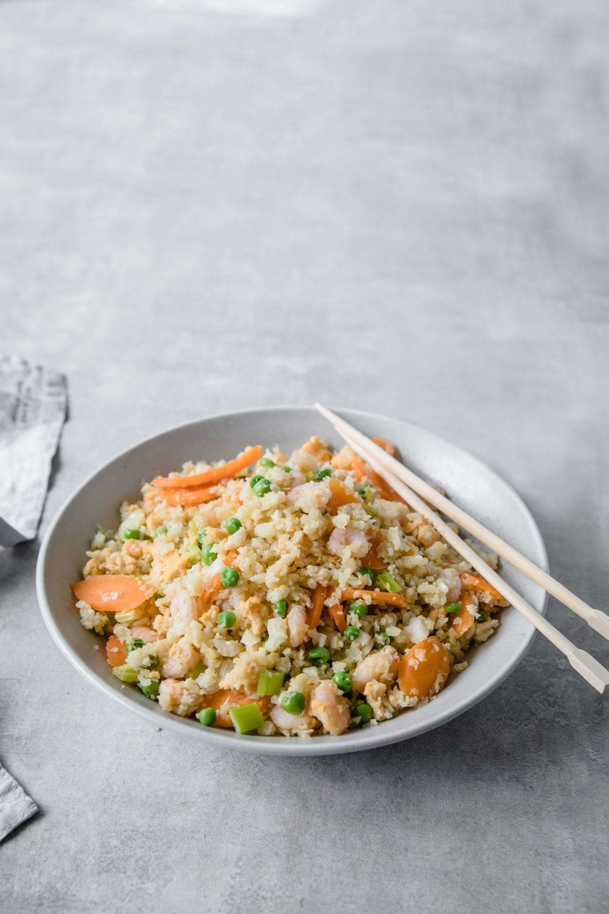 a white bowls filled with cauliflower fried rice with shrimp, carrots and peas