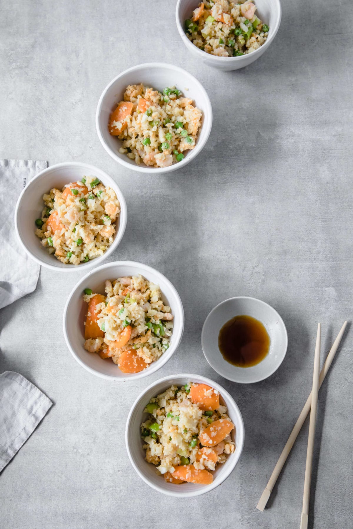 4 white bowls filled with cauliflower fried rice with shrimp, carrots and peas