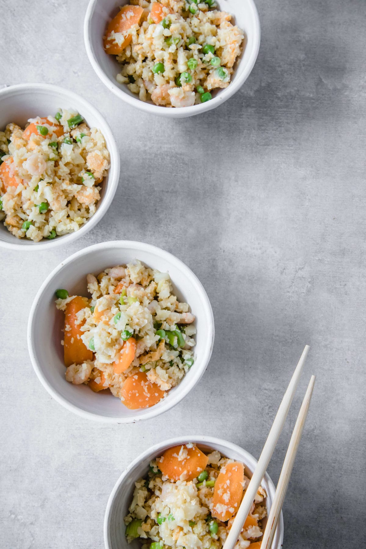 4 white bowls filled with cauliflower fried rice with shrimp, carrots and peas