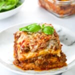a plate of low carb lasagna, garnish with fresh parsley, with a baking dish of lasagna behind it