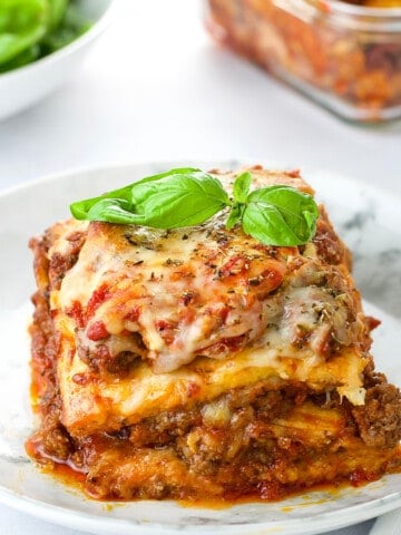 a plate of low carb lasagna, garnish with fresh parsley, with a baking dish of lasagna behind it