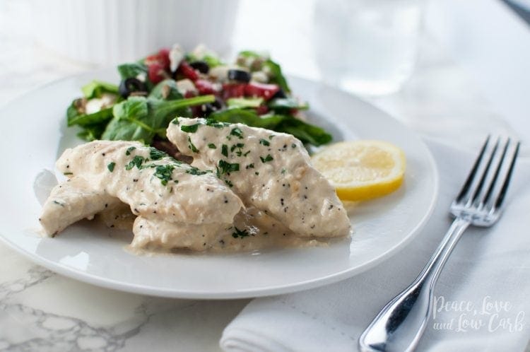 a white plate with creamy chicken, lemon slices and a mixed green salad