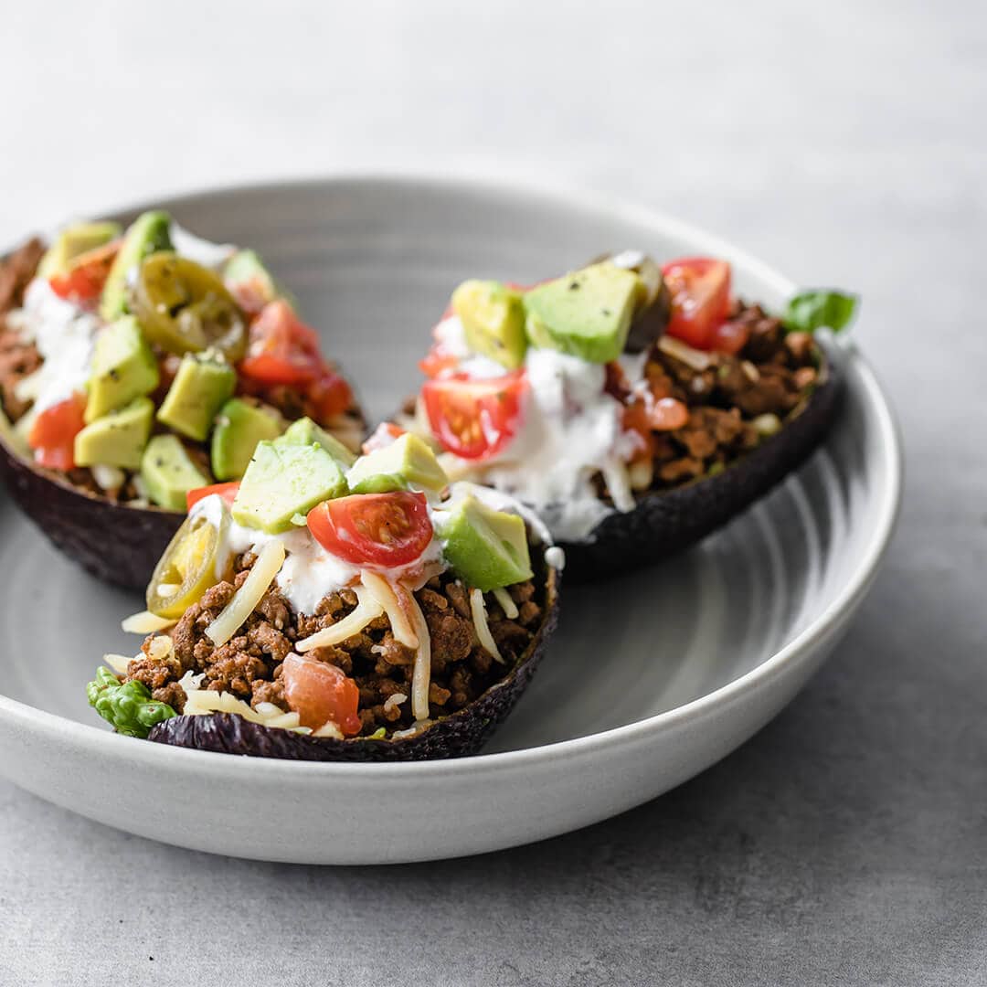 tacos served in an avocado shell with ground beef, cheese, tomatoes, avocado and sour cream 