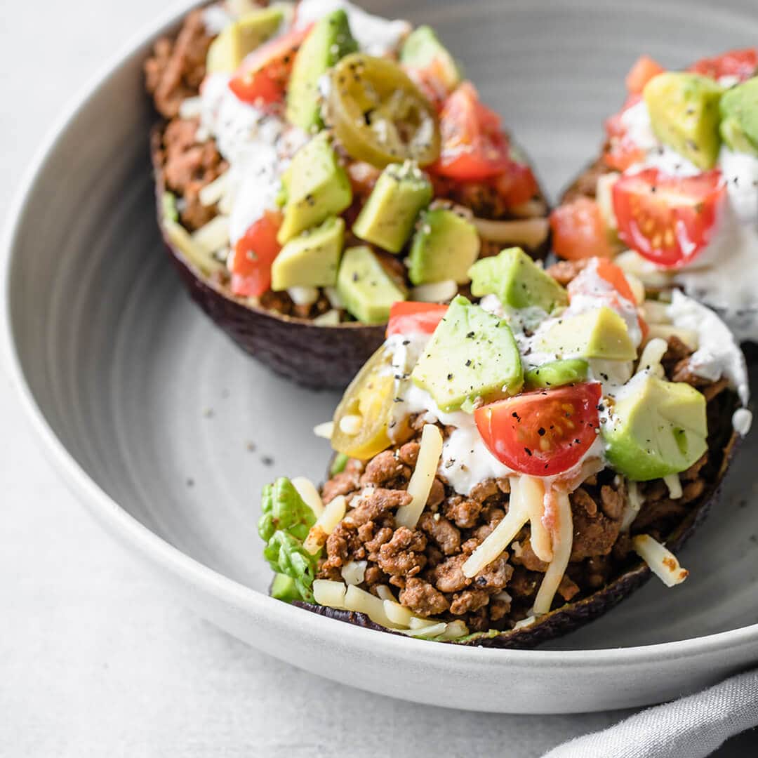 tacos served in an avocado shell with ground beef, cheese, tomatoes, avocado and sour cream 