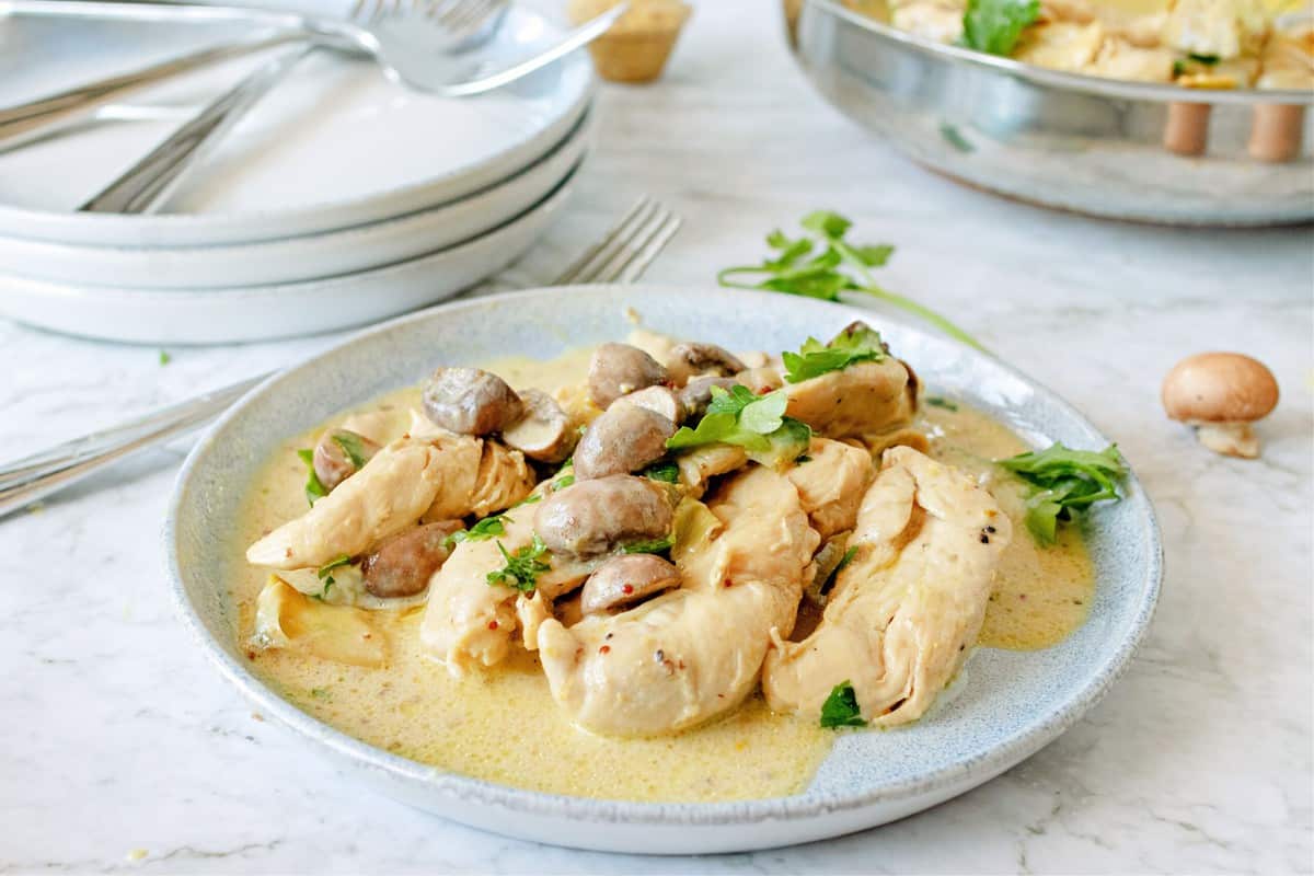 light blue plate with a portion of chicken dijon - chicken, mushrooms, artichokes, parsley and creamy mustard sauce