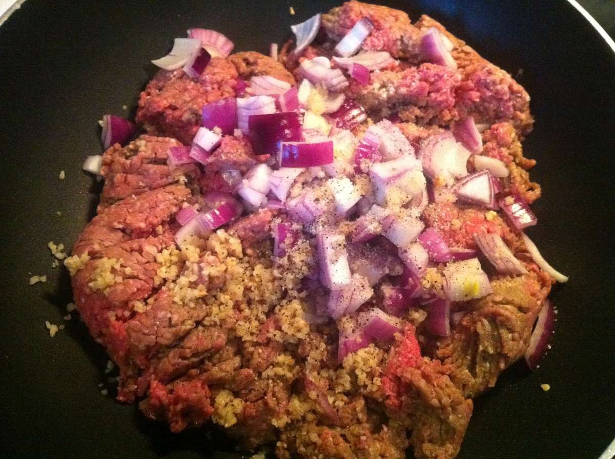 skillet with ground beef, red onions, garlic, and seasonings