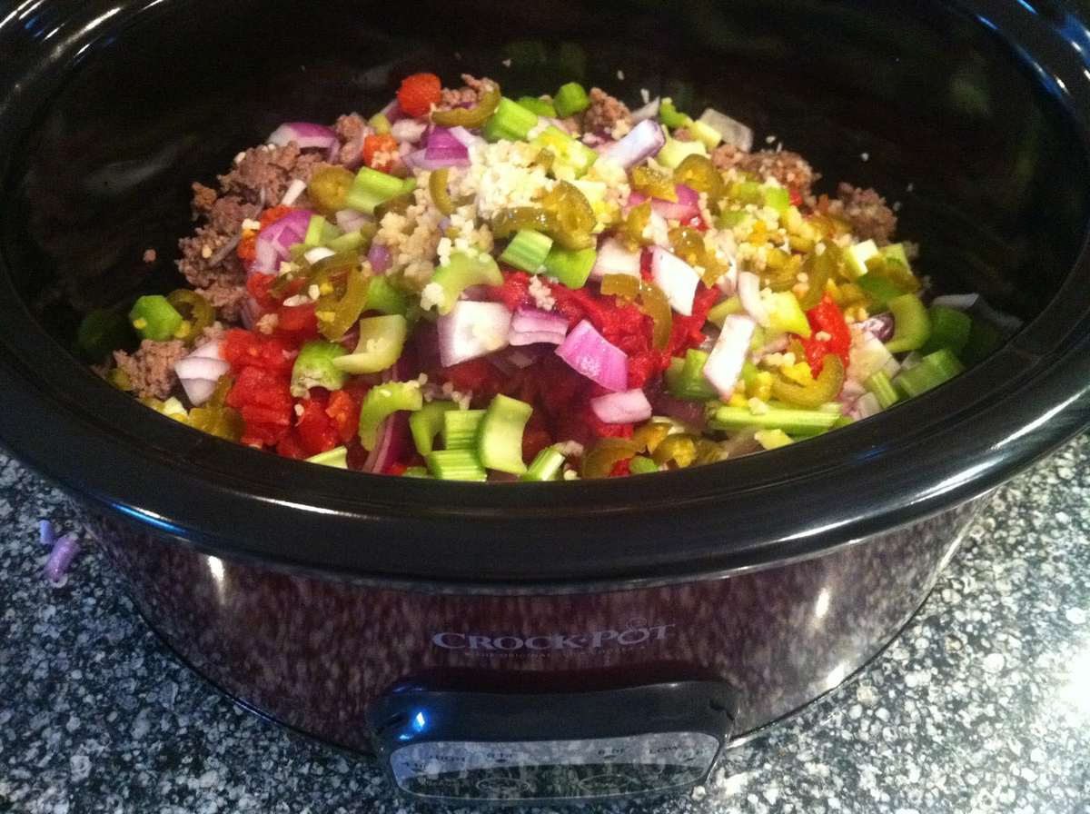 slow cooker with cooked ground beef, celery, onions, garlic, tomatoes, jalapeños, Worcestershire sauce to make beanless chili 