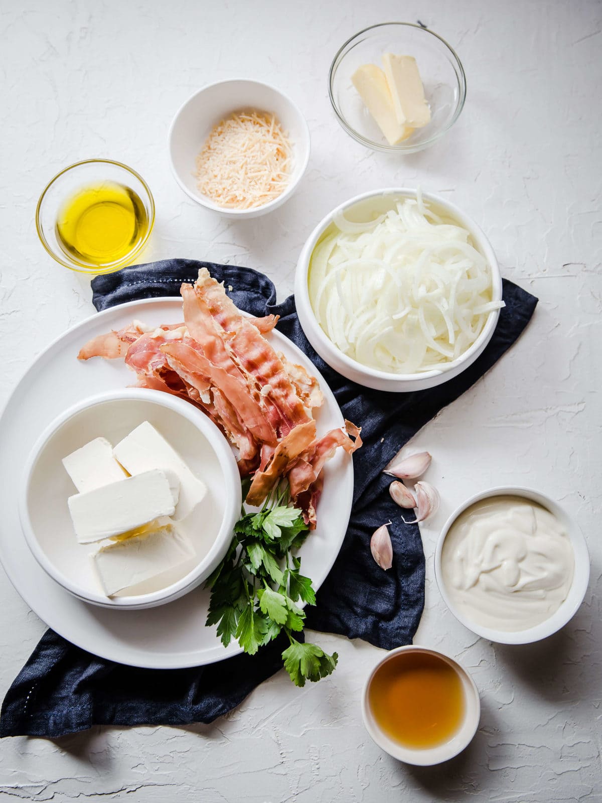 Ingredients laid out to make caramelized onion and bacon dip - onions, bacon, garlic, butter, olive oil, cheese and sour cream.