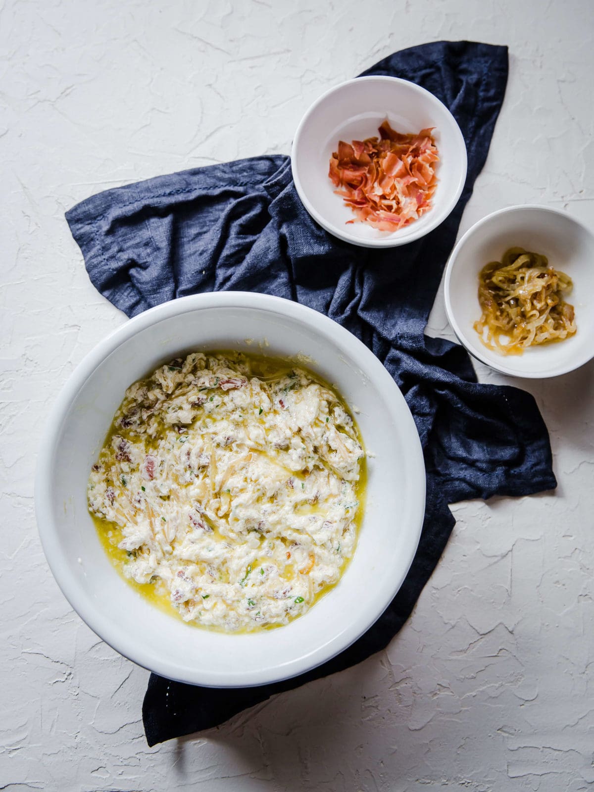 a bowl of caramelized onion dip with a small bowl of bacon and a small bowl of caramelized onions on the side.