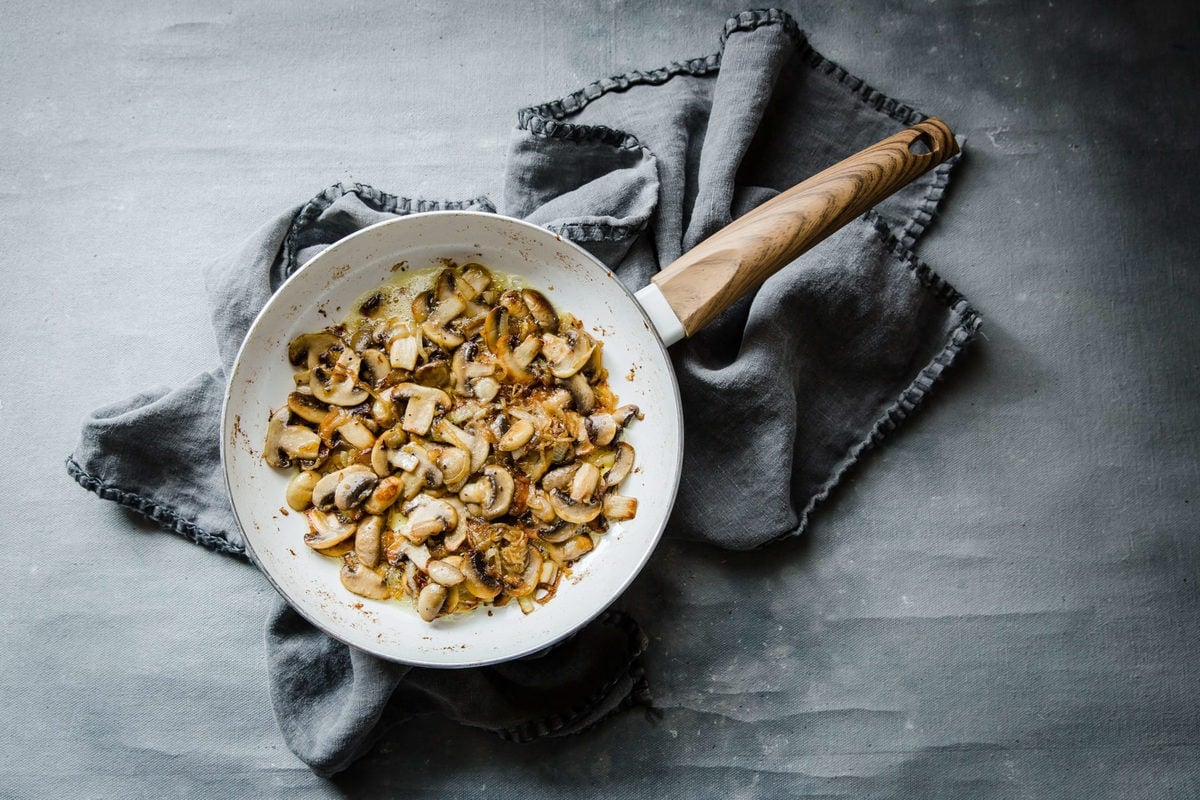 a gray tea towel and a ceramic skillet with sautéed mushrooms and onions