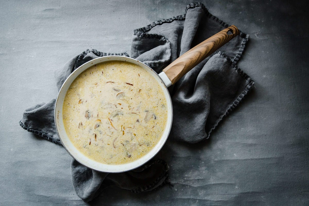 a sauce pan full of sour cream sauce with mushrooms and onions, and a gray towel.