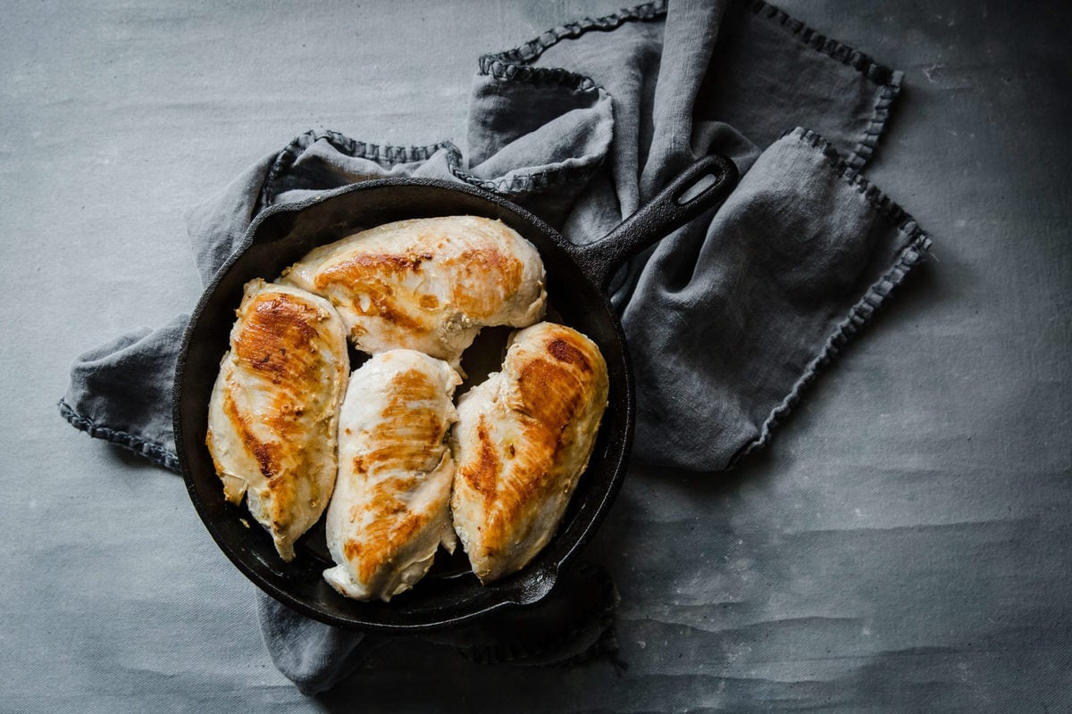 a gray towel and a cast iron skillet with four cooked chicken breasts