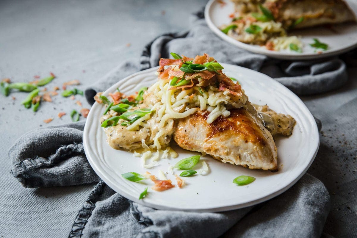 white plate with seared chicken, cheese, and a sour cream sauce with mushrooms and onions