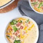 Overhead shot of a bowl of Cheddar Broccoli Soup garnished with cheddar, crispy ham and broccoli