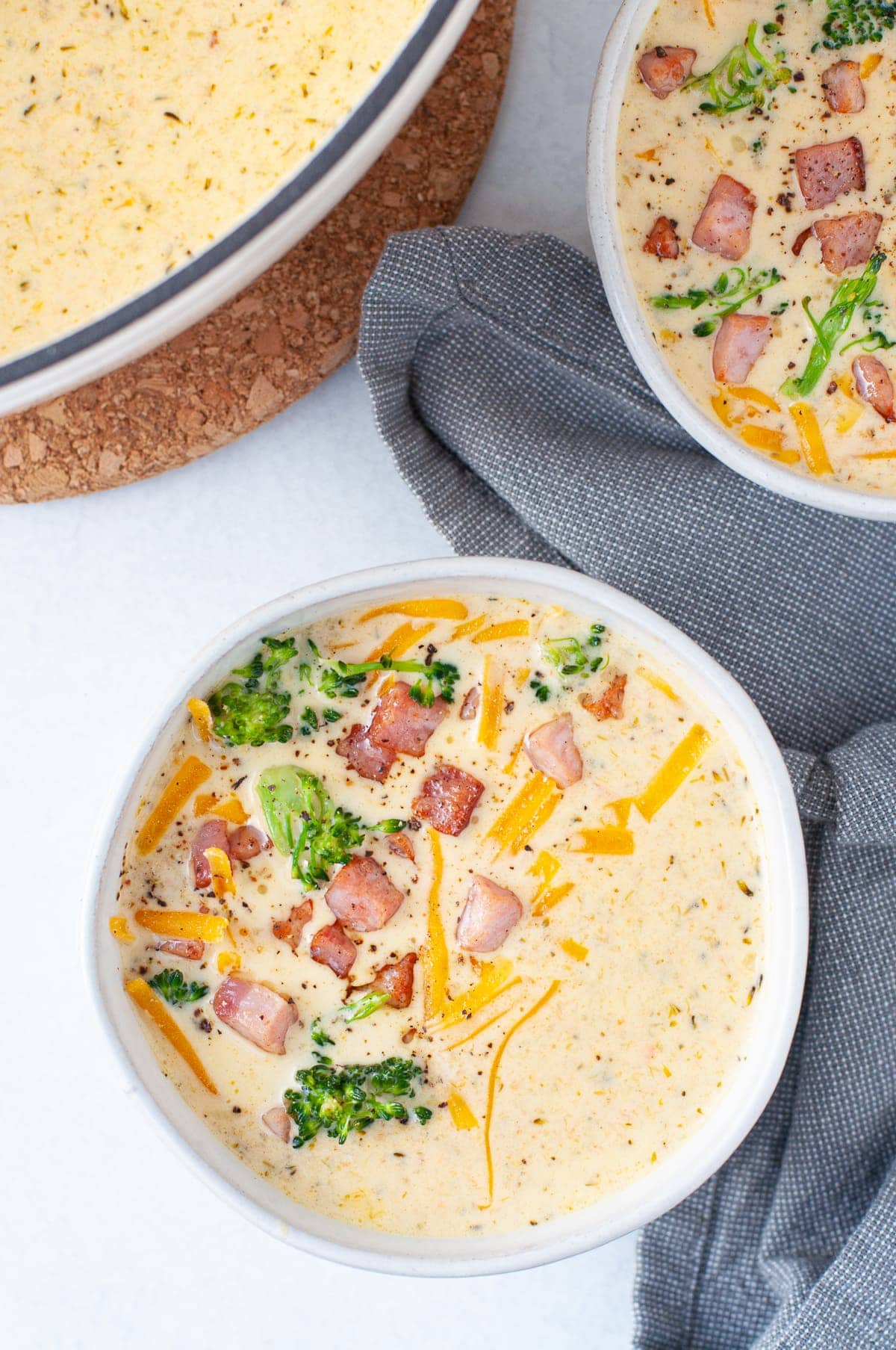 Overhead shot of a bowl of Cheddar Broccoli Soup garnished with cheddar, crispy ham and broccoli