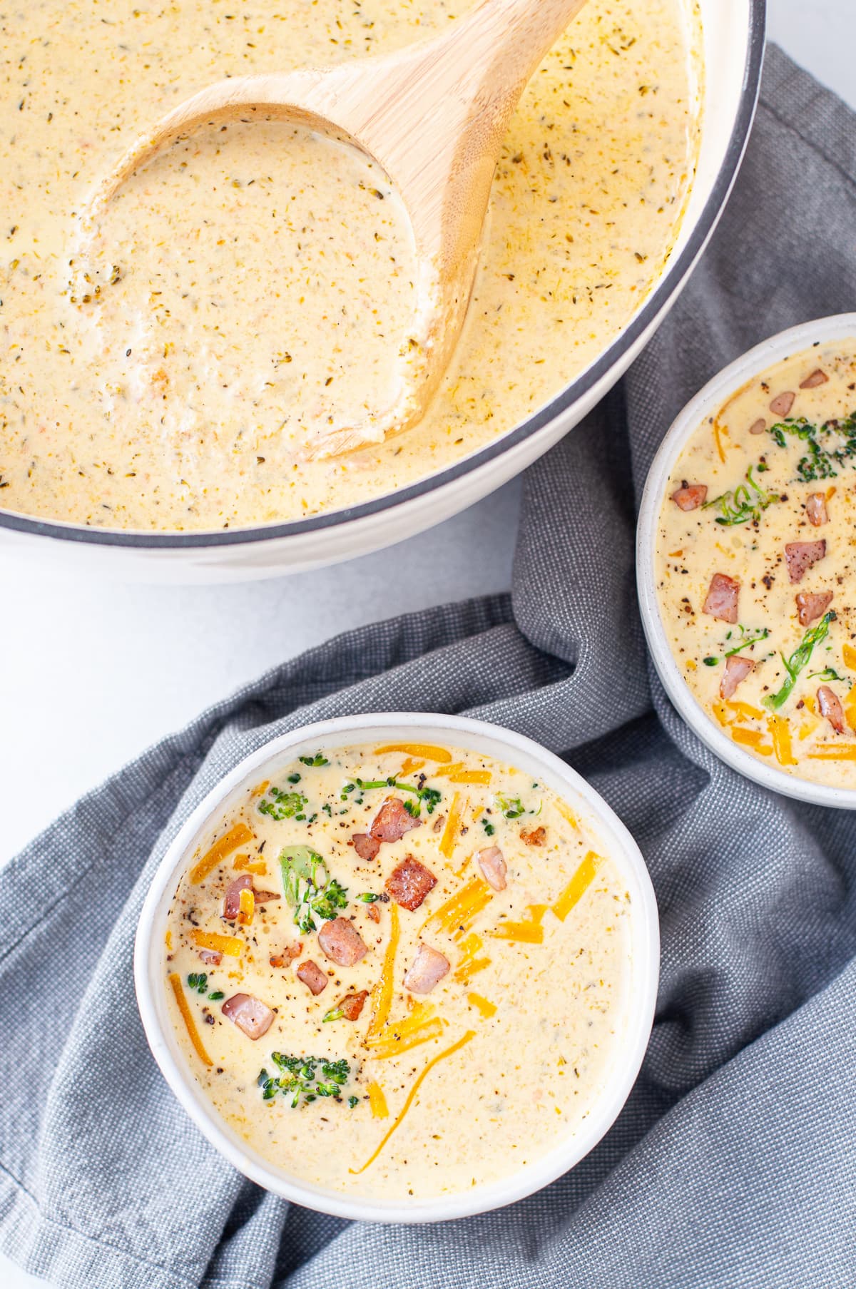 2 bowls of Keto Cheddar Broccoli Soup garnished with cheddar, crispy ham and broccoli