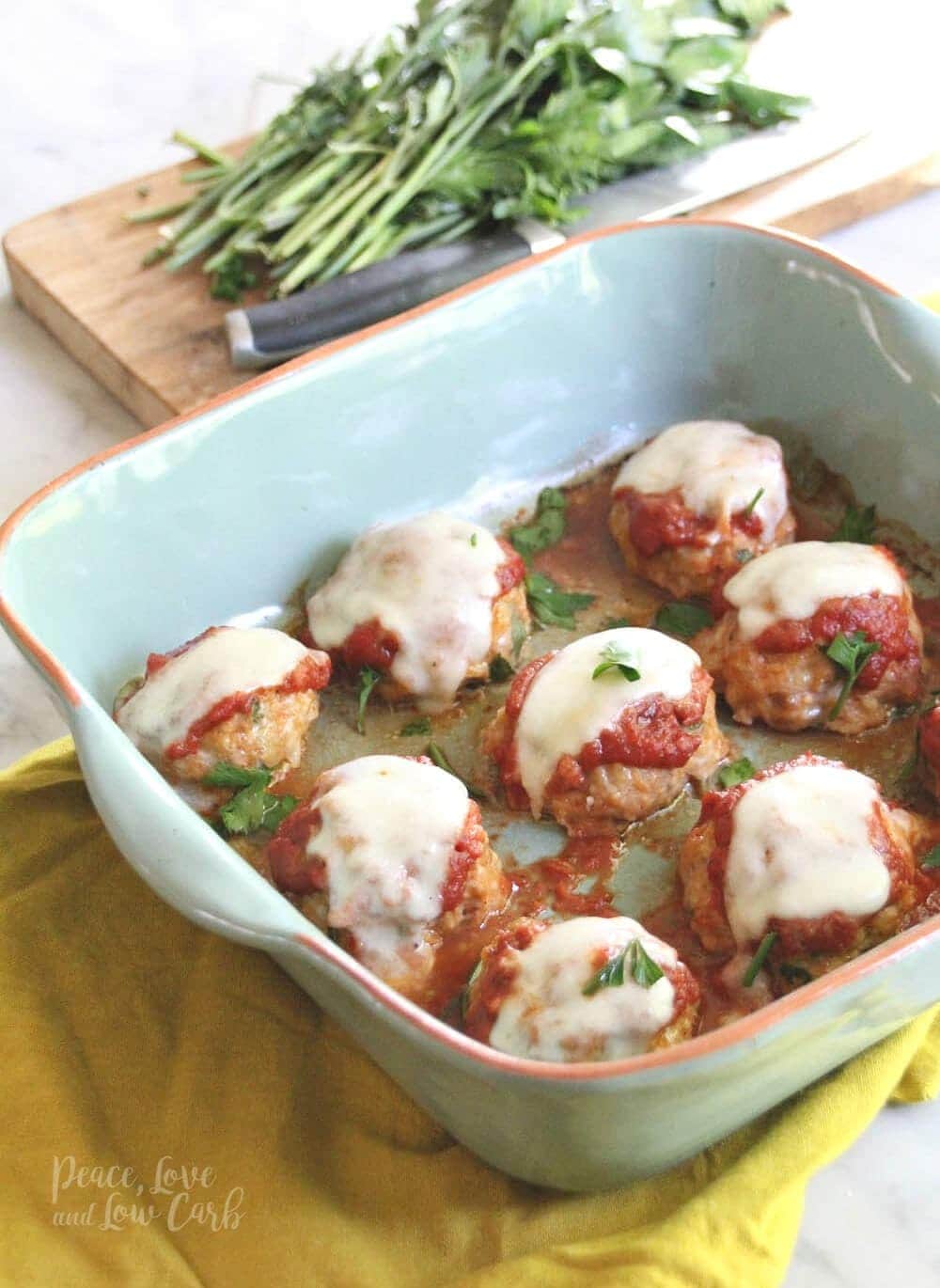 a baking dish full of chicken parmesan meatballs, topped with marinara sauce, melted mozzarella cheese, garnished with parsley 