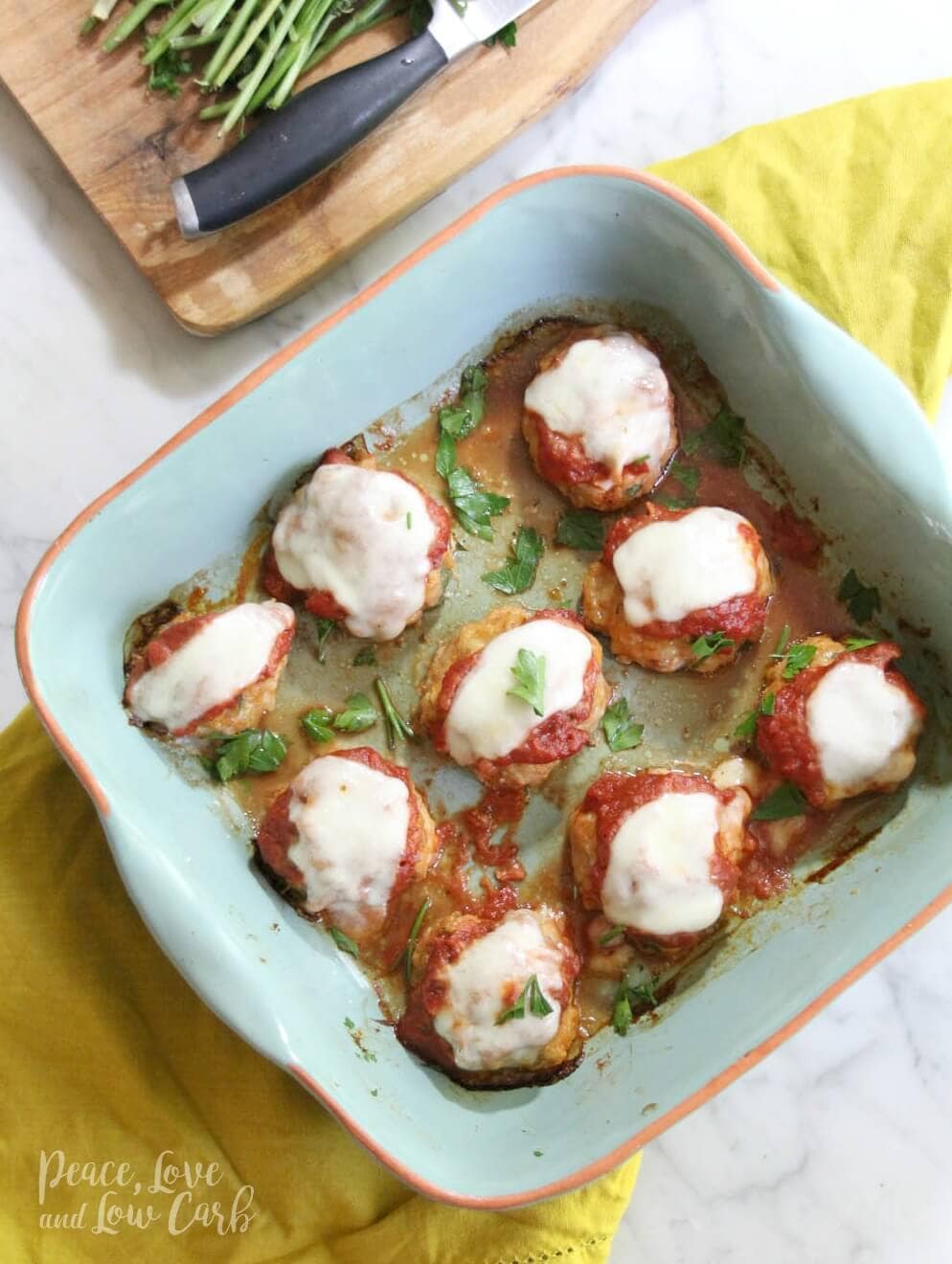 a baking dish full of chicken parmesan meatballs, topped with marinara sauce, melted mozzarella cheese, garnished with parsley 