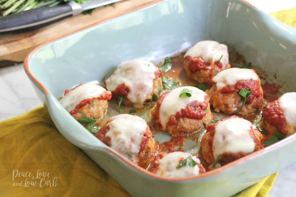 a baking dish full of chicken parmesan meatballs, topped with marinara sauce, melted mozzarella cheese, garnished with parsley 