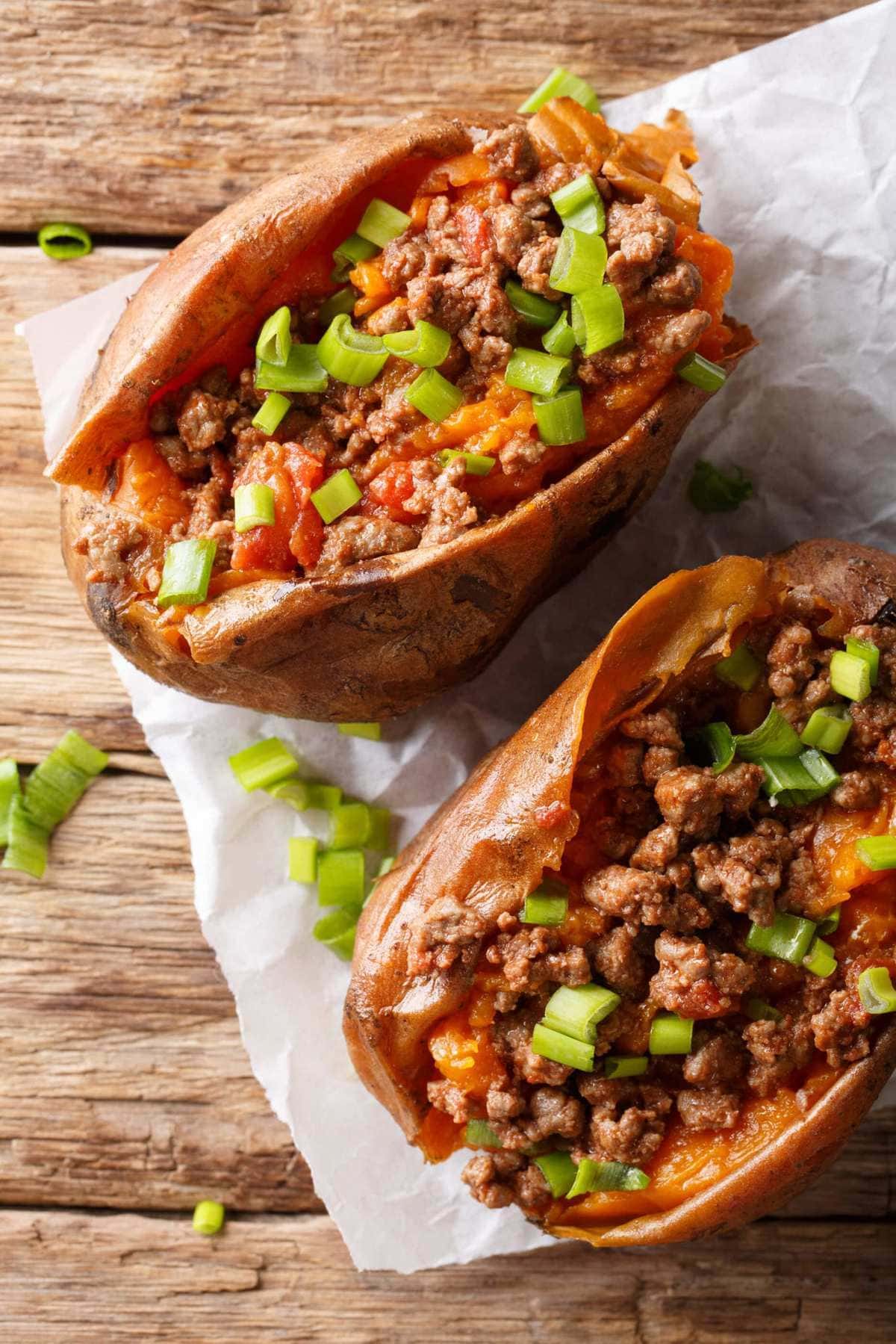 A cooked sweet potato, split open and stuffed with Sloppy Joe filling and topped with green onions.