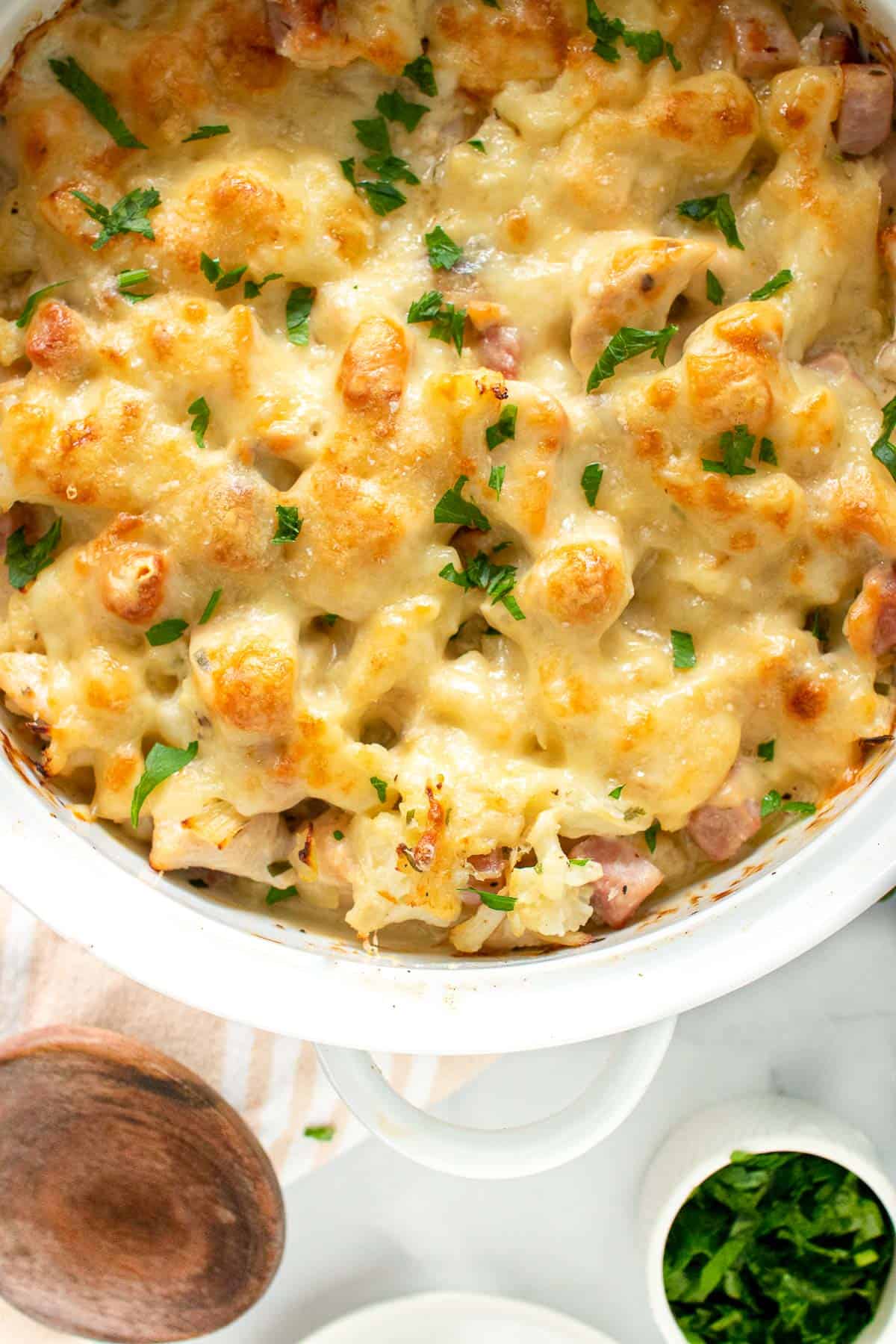 a white casserole dish full of a cheesy low carb chicken cordon blue casserole, garnished with parsley