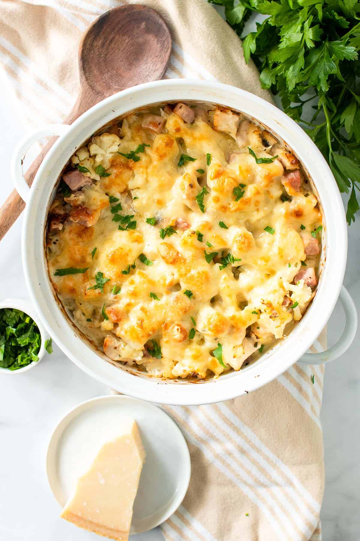 a white casserole dish full of a cheesy low carb chicken cordon blue casserole, garnished with parsley