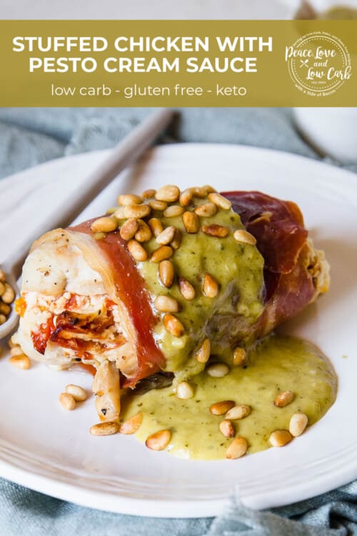 A serving plate with a chicken breast that is stuffed and then wrapped in prosciutto and topped with pesto cream sauce and toasted pine nuts.