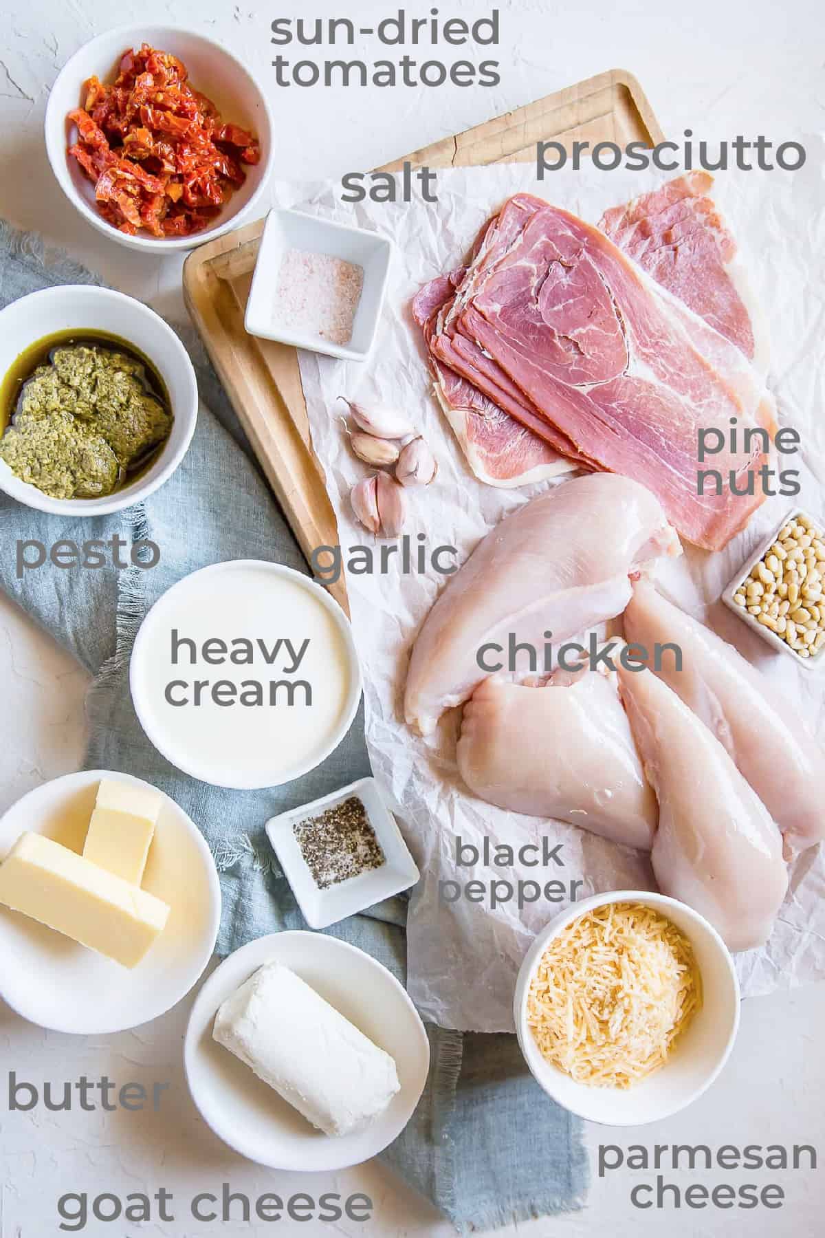 Ingredients all laid out to make a stuffed chicken breast recipe with prosciutto, goat cheese, sun-dried tomatoes, garlic, and cheese.