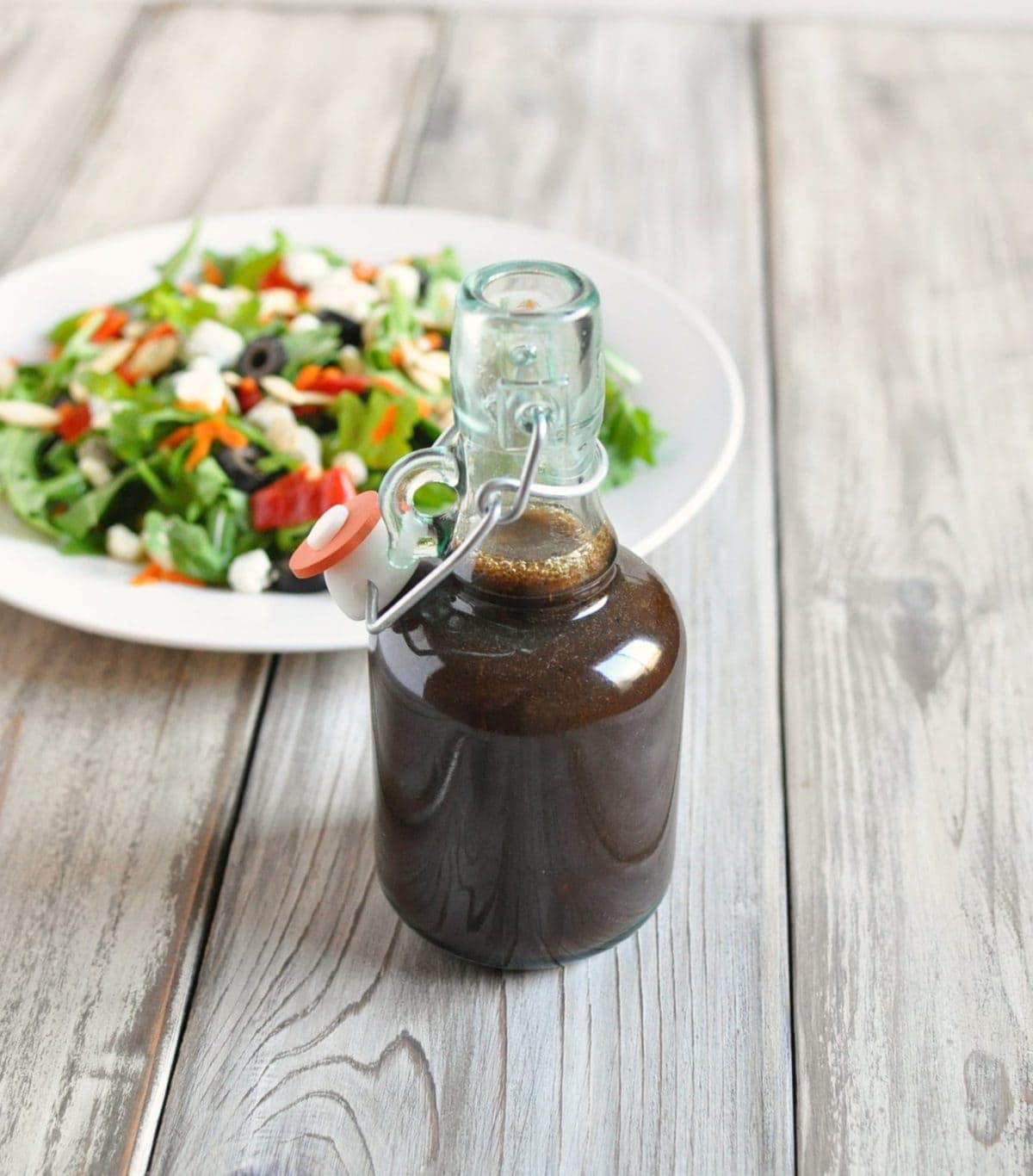 a jar of balsamic vinaigrette dressing with a mixed green salad in the background 