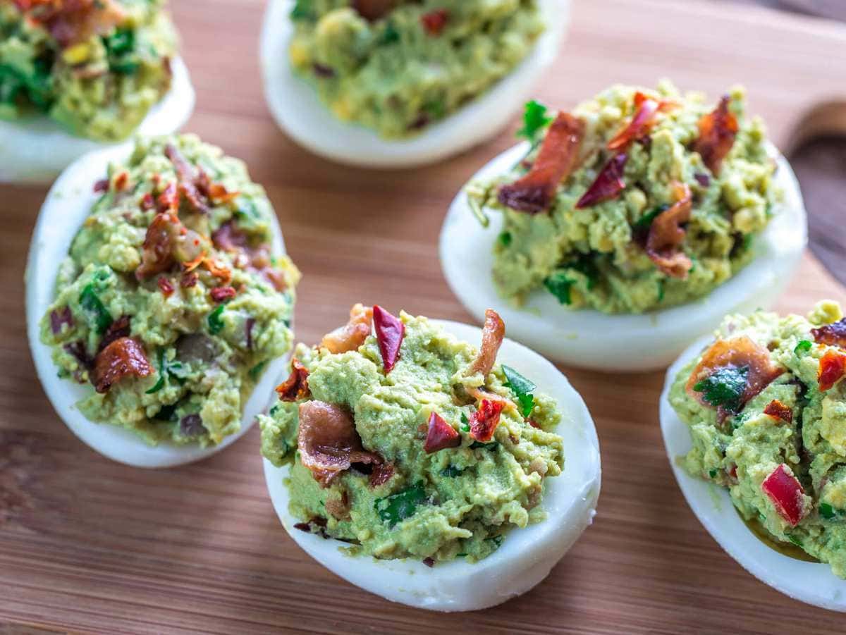 deviled eggs made with guacamole and bacon, served on a wooden tray