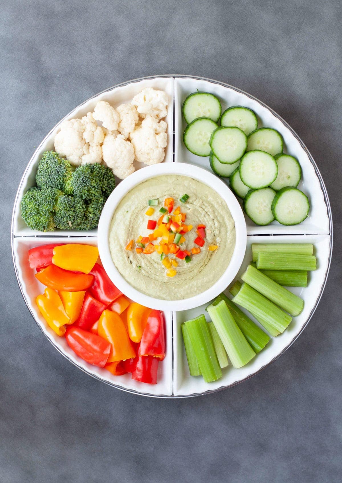 a white serving dish with fresh cucumbers, celery, peppers, cauliflower and broccoli served with low carb hummus.