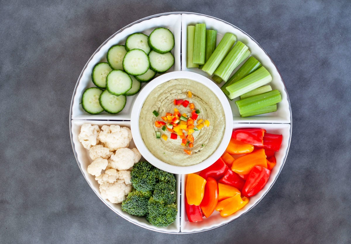 a white serving dish with fresh cucumbers, celery, peppers, cauliflower and broccoli served with low carb hummus.