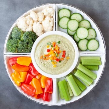 a white serving dish with fresh cucumbers, celery, peppers, cauliflower and broccoli served with low carb hummus.