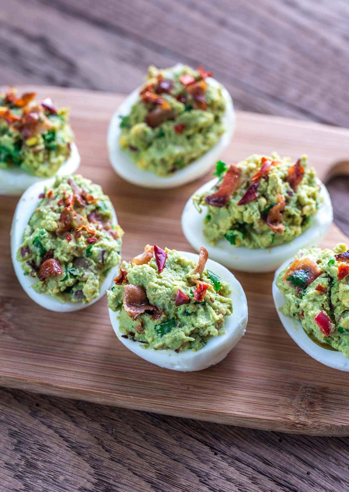deviled eggs made with guacamole and bacon, served on a wooden tray