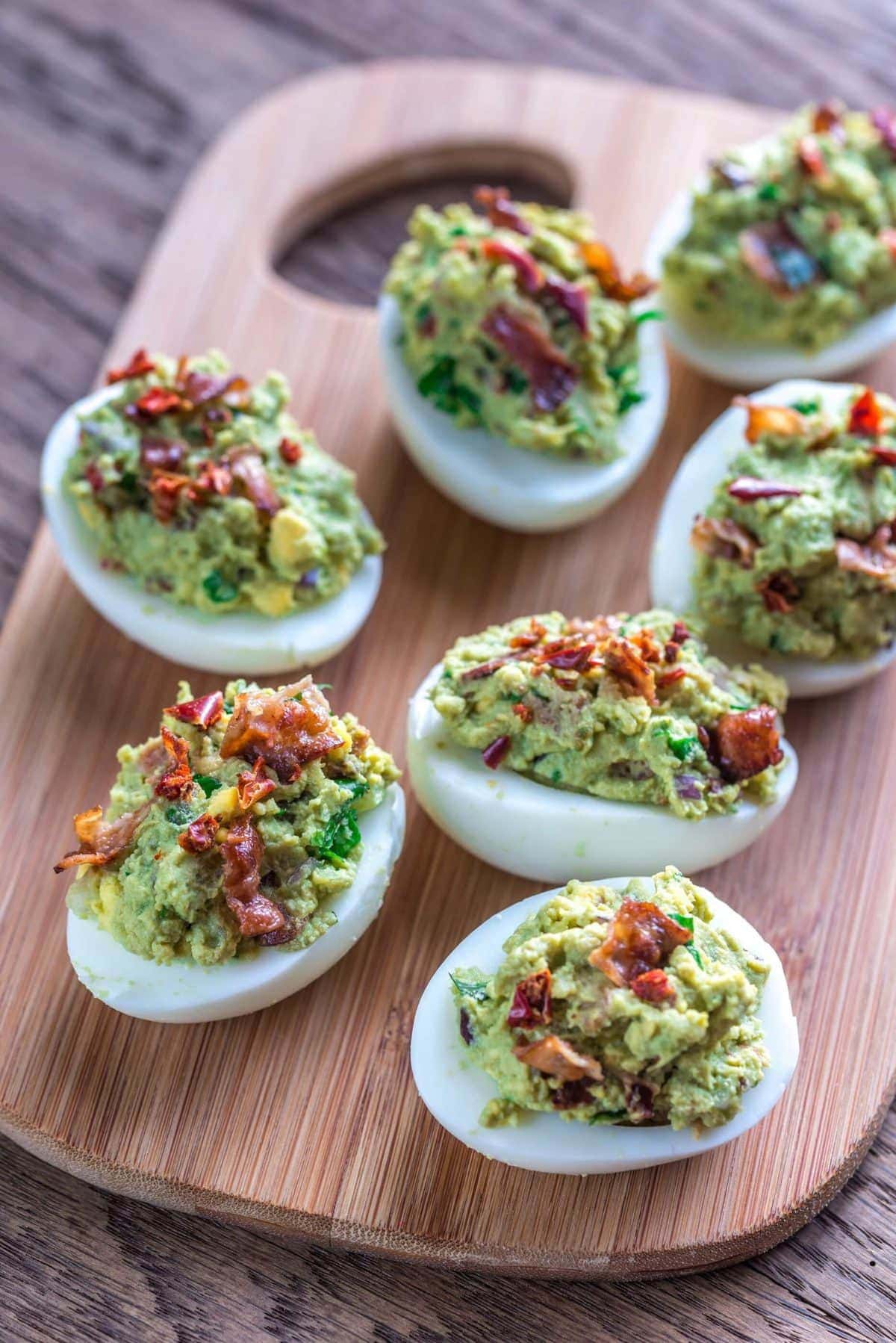 deviled eggs made with guacamole and bacon, served on a wooden tray