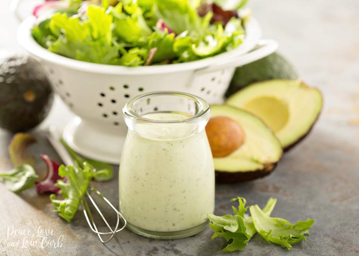 a jar of creamy salad dressing with lettuce and avocado behind it. 