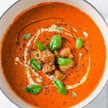 a dutch oven full of tomato bisque, garnished with keto croutons, fresh basil and a swirl of cream
