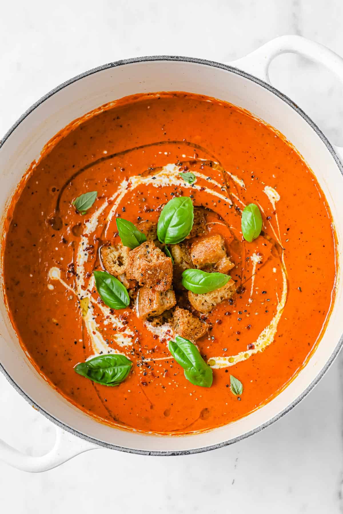 a dutch oven full of tomato bisque, garnished with keto croutons, fresh basil and a swirl of cream