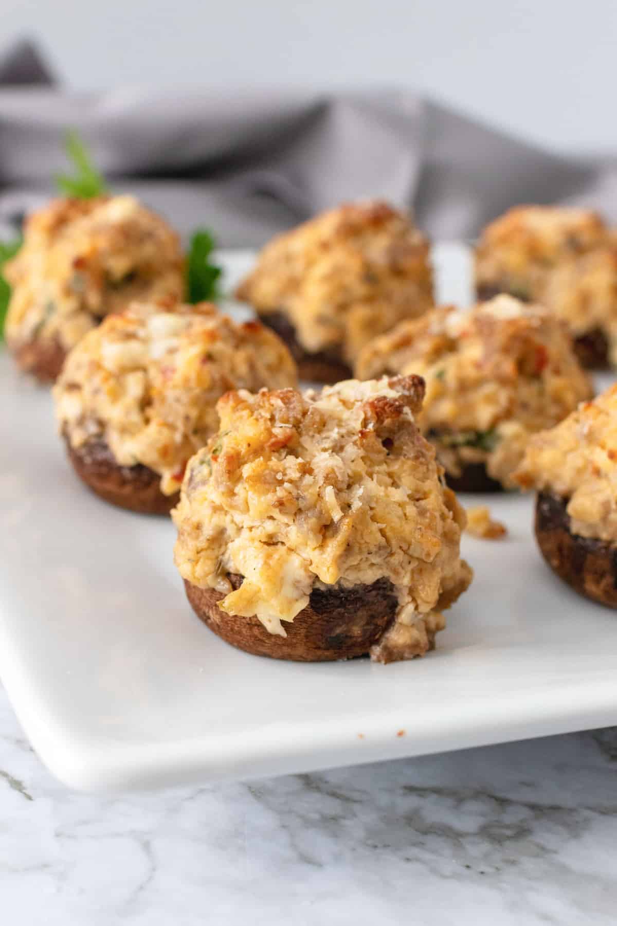 Sausage stuffed mushrooms on a white plate, garnishes with parsley