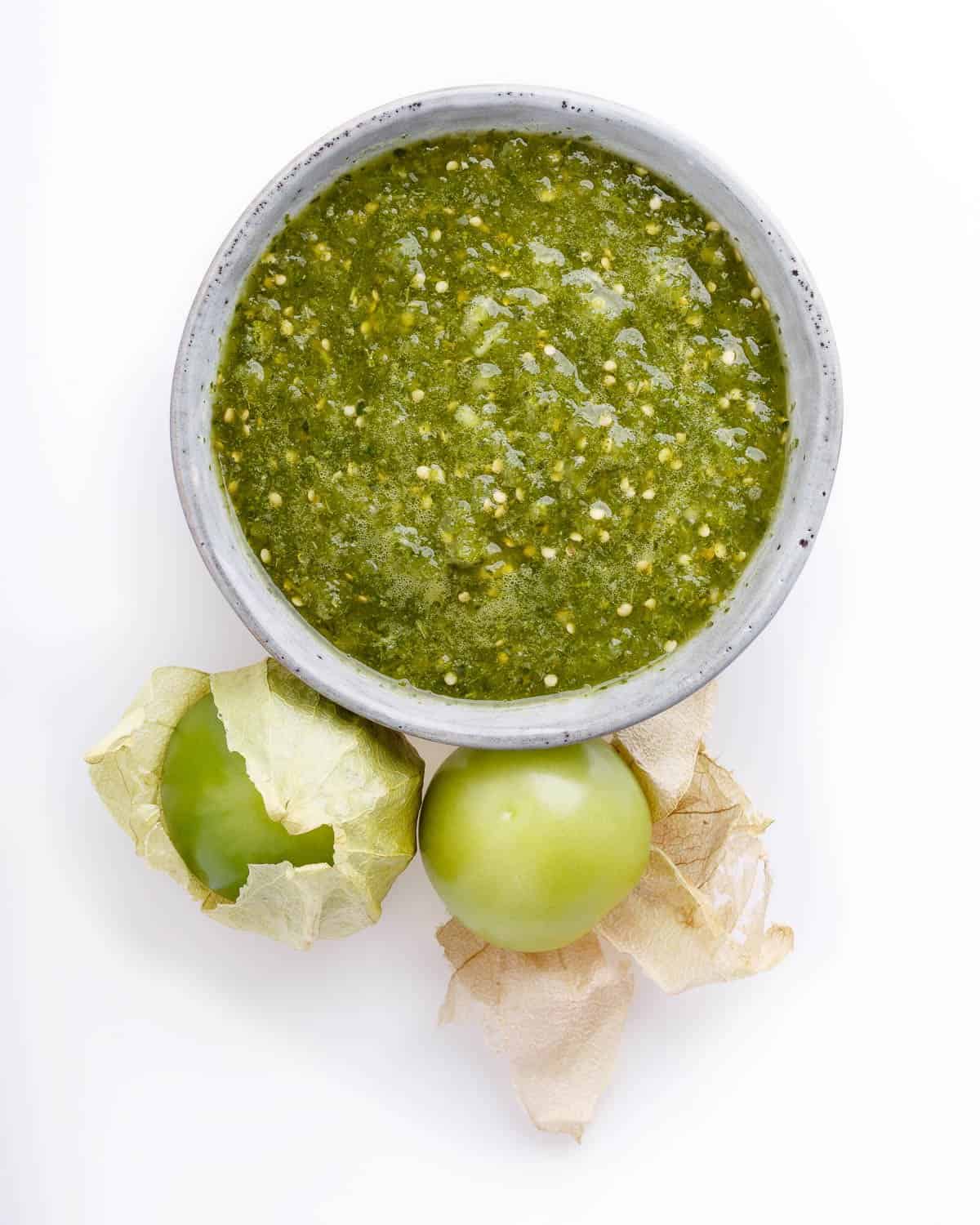 small gray ceramic bowl filled with salsa verde, with 2 husked tomatillos beside it