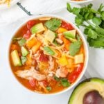 Overhead shot of a bowl of chicken fajita soup, topped with avocado, cilantro, cheese, and bell peppers