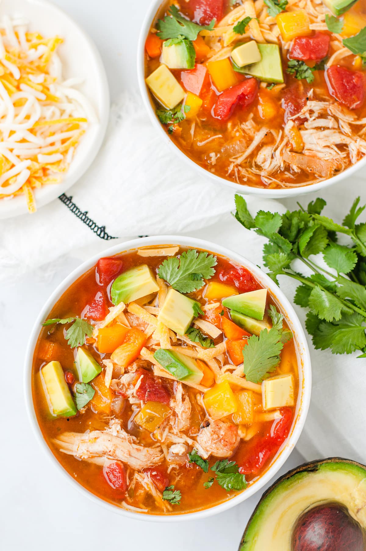 Overhead shot of a bowl of chicken fajita soup, topped with avocado, cilantro, cheese, and bell peppers