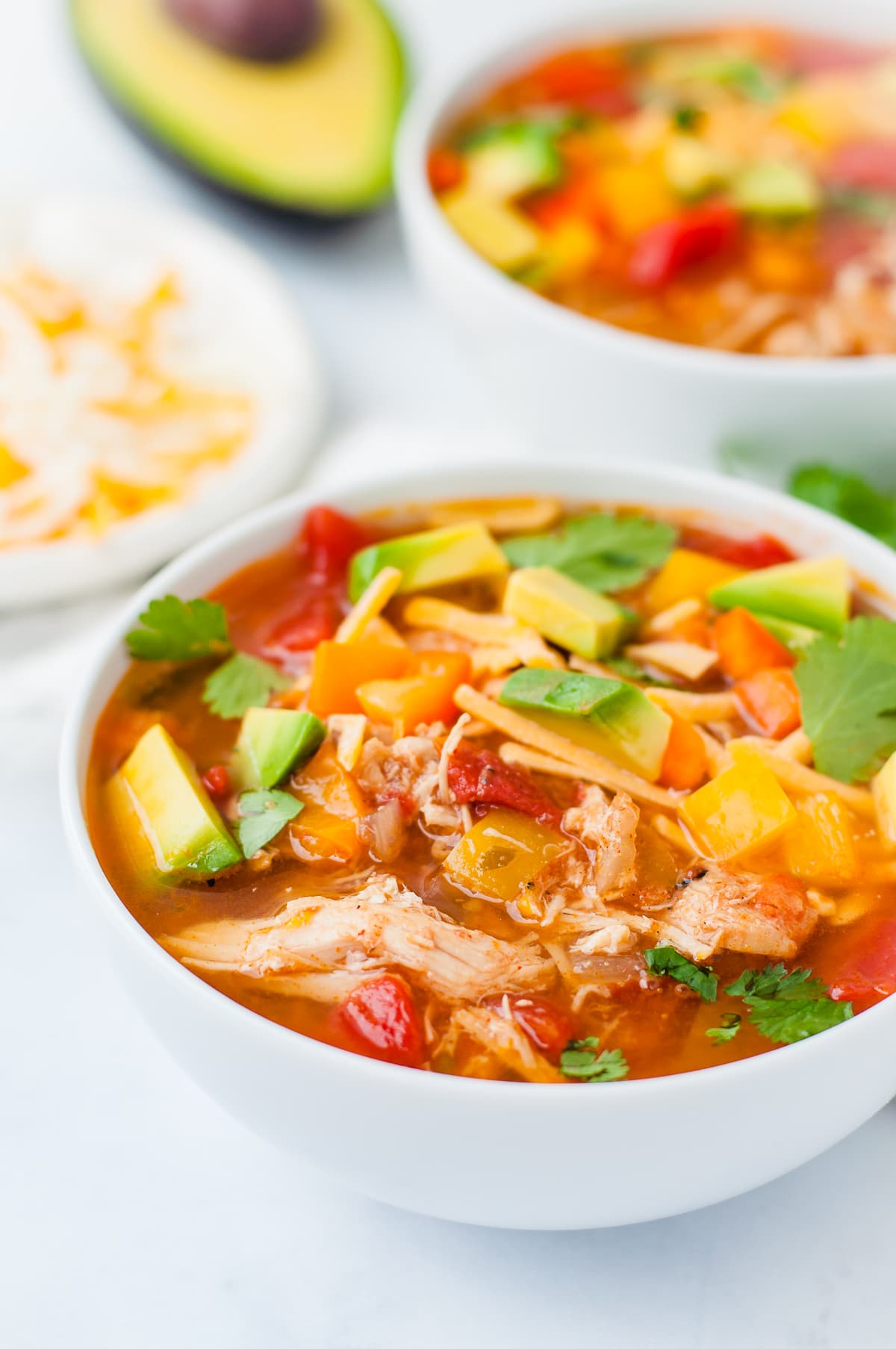 Overhead shot of a bowl of chicken fajita soup, topped with avocado, cilantro, cheese, and bell peppers