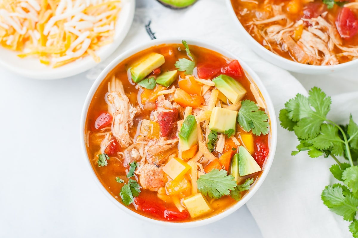 Overhead shot of a bowl of chicken fajita soup, topped with avocado, cilantro, cheese, and bell peppers